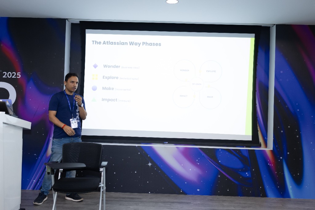Dushyant Sharma on stage presenting The Atlassian Way phases — Wonder, Explore, Make, Impact — at the ACE Delhi-Gurugram conference.