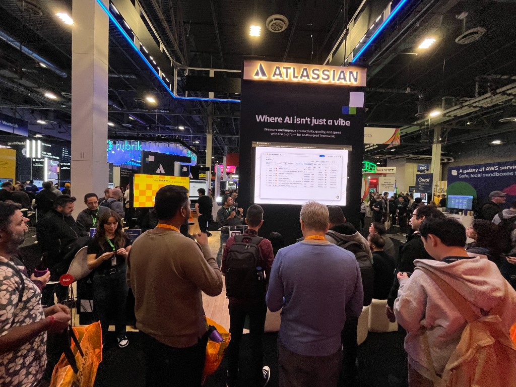 Atlassian booth at AWS re:Invent 2025 with attendees watching the live demo on the main screen.